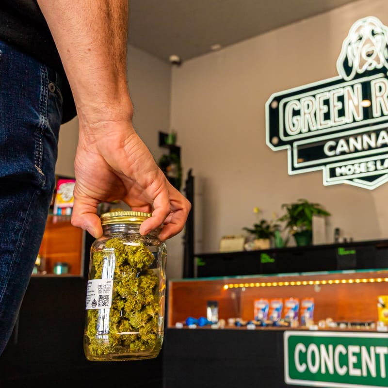 customer holding jar of cannabis flower for purchase with green roads neon sign in background