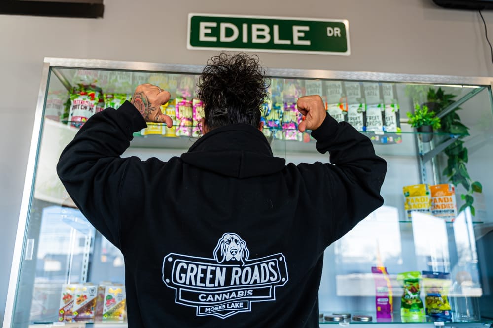 personality employee points to green roads cannabis logo on back of sweatshirt