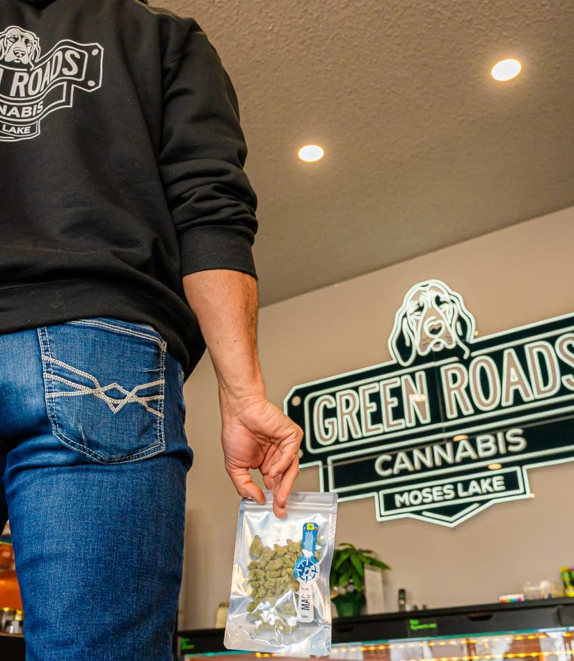 quality-and-education customer holding package of cannabis flower for purchase with green roads neon sign in background